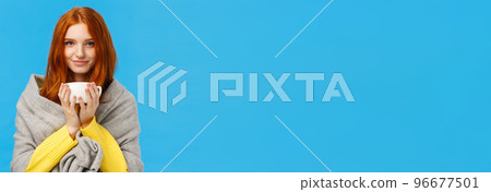 Lovely, romantic good-looking redhead female in grey scarf, getting warm, drinking hot tea, holding cup of coffee, smiling camera delighted and relaxed, standing blue background pleased 96677501