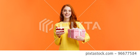 Holidays, celebration and people concept. Cheerful gorgeous redhead girlfriend receive cute gift, holding present in wrapped box and piece cake with candle, smiling celebrate birthday, b-day party 96677584
