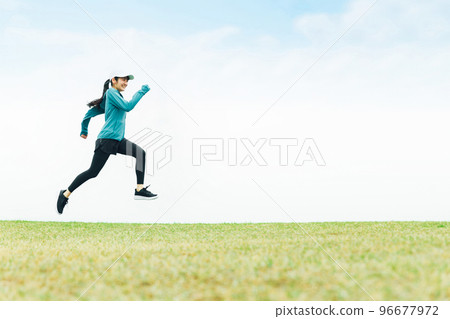 身穿運動服的亞洲女性在草地上跳躍時奔跑 96677972