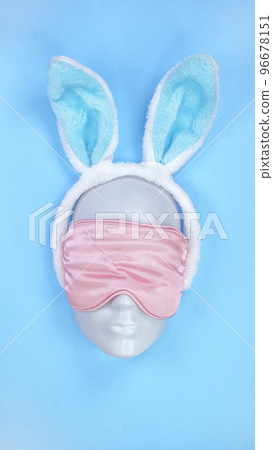 Pink sleeping eye mask on mannequin face with blue fluffy Easter bunny ears on blue background, sleeping disorder. Holidays, Head accessory. Plastic face. Pink sleeping eye mask on mannequin face with blue fluffy Easter bunny ears on blue background, sleeping disorder. Holidays, Head accessory. Plastic face. 96678151