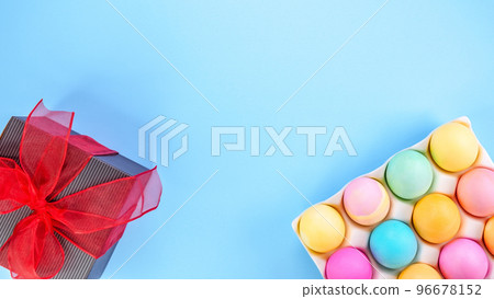 Easter pastel background with colorful eggs and a gift box with red bow on a blue background. The concept of a Happy Easter. Top view, copy space. 96678152