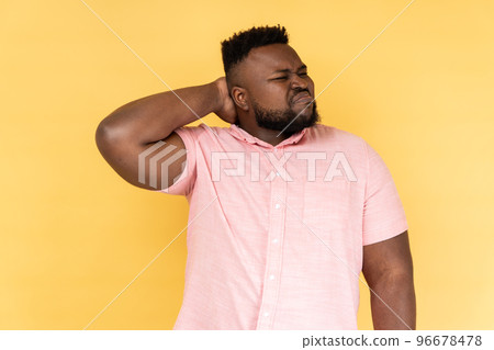 Portrait of worried anxious bearded man wearing pink shirt touching neck, feeling acute pain moving and turning head, suffering spine problems. Indoor studio shot isolated on yellow background. Portrait of worried anxious bearded man wearing pink shirt touching neck, feeling acute pain moving and turning head, suffering spine problems. Indoor studio shot isolated on yellow background. 96678478