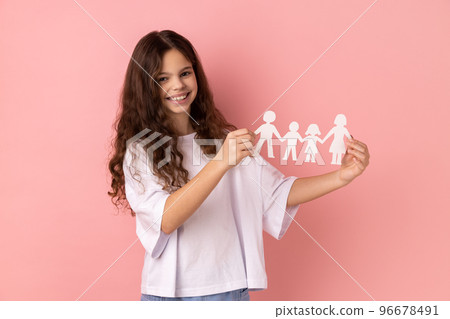 Portrait of smiling charming little girl wearing white T-shirt holding paper chain people in hands, happy family, relationships, childhood. Indoor studio shot isolated on pink background. Portrait of smiling charming little girl wearing white T-shirt holding paper chain people in hands, happy family, relationships, childhood. Indoor studio shot isolated on pink background. 96678491