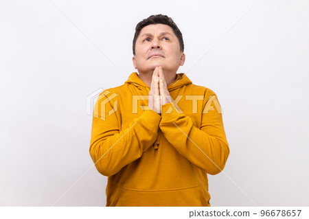 Portrait of handsome middle aged man praying up heartily, feeling guilty, pleading begging help from heaven, wearing urban style hoodie. Indoor studio shot isolated on white background. 96678657