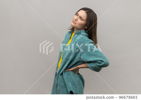 Portrait of frustrated anxious unhealthy woman holding hands on lower back, kidney injury, backache, wearing casual style jacket. Indoor studio shot isolated on gray background. Portrait of frustrated anxious unhealthy woman holding hands on lower back, kidney injury, backache, wearing casual style jacket. Indoor studio shot isolated on gray background. 96678665