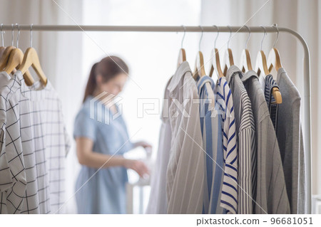 Young beautiful woman stands near the closet and hangs up her clothes. Clothes storage. Young beautiful woman stands near the closet and hangs up her clothes. Clothes storage. 96681051