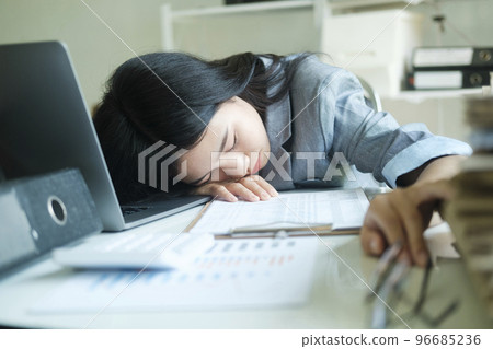 Young asian Business woman tired woman sleeping on desk with laptop at workplace alone. 96685236