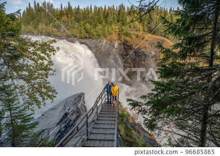 Couple standing on viewpoint bridge waterfall Tannforsen northern Sweden, rainbow in mist rapid flowing cascades water Couple standing on viewpoint bridge waterfall Tannforsen northern Sweden, rainbow in mist rapid flowing cascades water 96685865