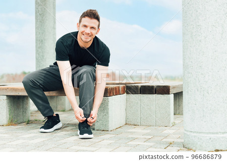 Smiling Caucasian man wearing sportswear tying shoelaces to prepare for and warm up for exercise Smiling Caucasian man wearing sportswear tying shoelaces to prepare for and warm up for exercise 96686879