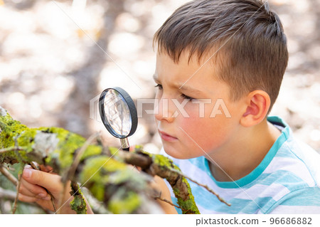 Curious boy is exploring nature with magnifying glass outdoors 96686882