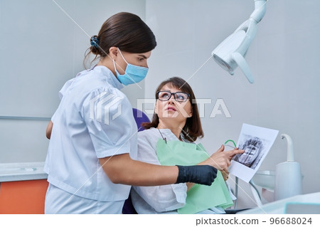 Female dentist talking to woman patient, discussing x-rays of teeth and jaws 96688024