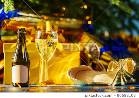 a bottle of champagne, a glass of drink and sandals under the Christmas tree. a bottle of champagne, a glass of drink and sandals under the Christmas tree. 96688108