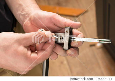 The craftsman holds a door handle and a hex key in his hands, installing a door handle. 96688945