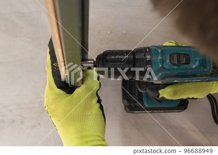 Drilling a hole in the door with a green screwdriver, close-up of the drilling process. Drilling a hole in the door with a green screwdriver, close-up of the drilling process. 96688949