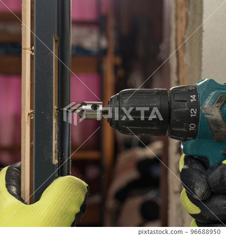 The craftsman drills a hole in the door frame for subsequent attachment to the wall. The craftsman drills a hole in the door frame for subsequent attachment to the wall. 96688950