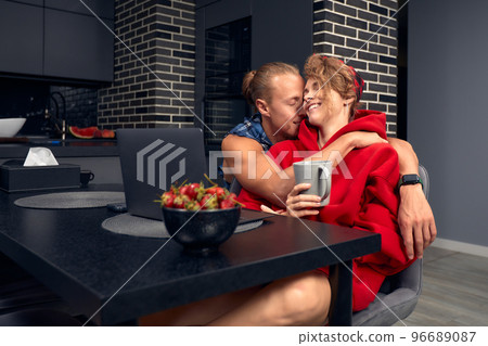 Engaged couple has breakfast together in their new home - young couple smiling while drinking and eating in the kitchen. Engaged couple has breakfast together in their new home - young couple smiling while drinking and eating in the kitchen. 96689087