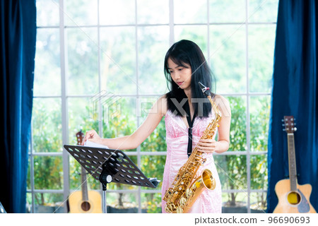 Young woman saxophonist with an instrument stands by the window. Cozy home interior. Concept of hobbies, inner world, development of talents, music school. Young woman saxophonist with an instrument stands by the window. Cozy home interior. Concept of hobbies, inner world, development of talents, music school. 96690693