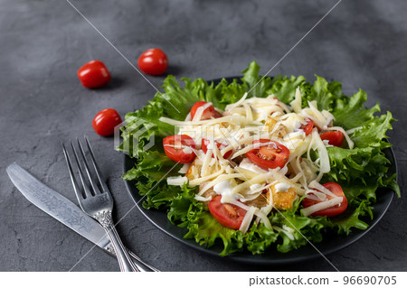 Traditional caesar salad with chicken on a black plate on black table with napkin fork and knife. 96690705