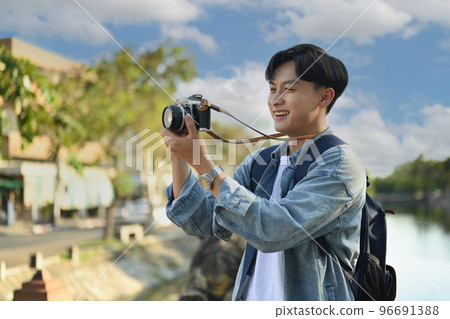 Young hipster man traveler taking pictures with camera while standing on bridge over a river in the city  96691388