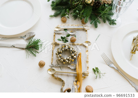 Top view of a festive Christmas table setting on a white background with a decorated pine branch, glass cutting Board, and a wreath of bells 96691533