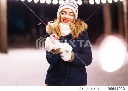 Cheerful young woman holding a sparkler in hand in forest. Woman happiness and playing firework. 96691920