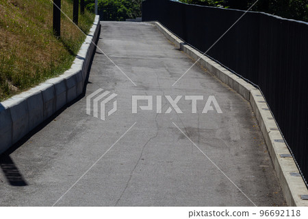 The edge of a park paved road, separated by a curb with a lawn. Fallen yellow autumn leaves on the road and lawn. Spots of light on the road 96692118