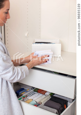 Caucasian young woman puts clothes in the closet. Magic of Tidying Up. Caucasian young woman puts clothes in the closet. Magic of Tidying Up. 96693189