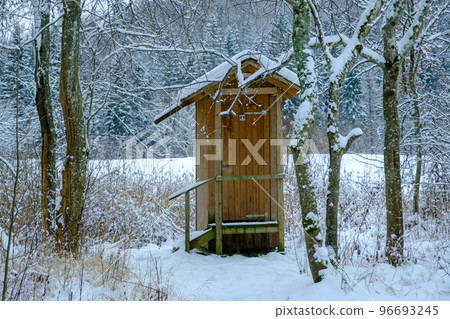 Outdoor wooden toilet house covered with snow on winter forest and trees background. Among the trees by the tourist trail Outdoor wooden toilet house covered with snow on winter forest and trees background. Among the trees by the tourist trail 96693245