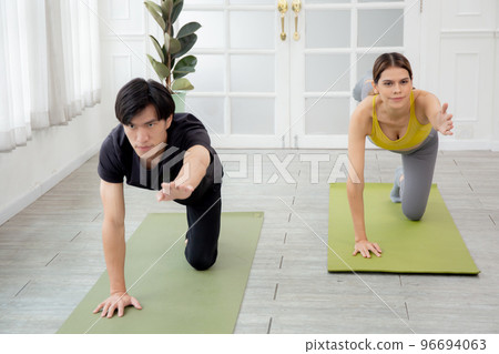 Young woman and man practicing workout with posing plank while stretching hands and leg. Young woman and man practicing workout with posing plank while stretching hands and leg. 96694063