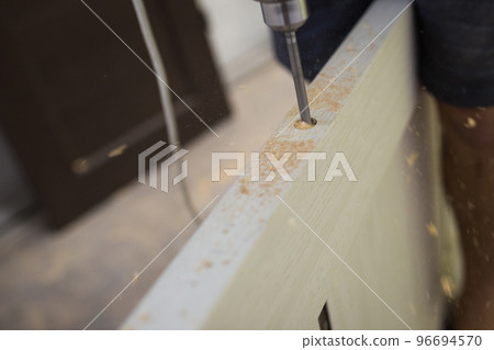 Drilling a hole in the furniture to install a lock on the door close-up. 96694570