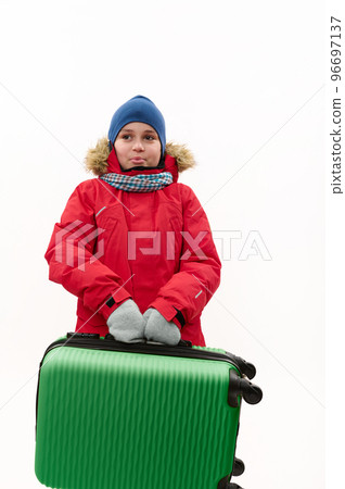 Happy multi-ethnic traveler child boy, wearing warm red down jacket, holding a green suitcase, going for winter vacations, isolated over white background with free advertising space. Kids travelling Happy multi-ethnic traveler child boy, wearing warm red down jacket, holding a green suitcase, going for winter vacations, isolated over white background with free advertising space. Kids travelling 96697137