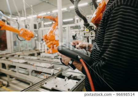 Technical engineer adjusting a robotic arm in the industrial automotive hall, industry concept 96698514