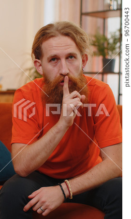 Young man presses finger to lips makes silence hush sign do not tells gossip secret, quiet at home Young man presses finger to lips makes silence hush sign do not tells gossip secret, quiet at home 96700443