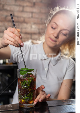 Young beautiful female bartender mixing a cocktail in a high glass. 96701125