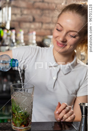 Young beautiful female bartender adds soda to a cocktail glass. 96701128