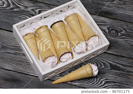 Wafer cones filled with marshmallows. Packed in a wooden tray. Homemade zephyr. On pine boards. Taken from above. 96701175