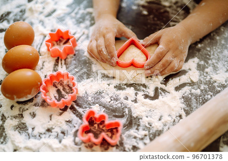 A little child cutting out shapes heart dough. Easter baking preparation. A craft for children. A little child cutting out shapes heart dough. Easter baking preparation. A craft for children. 96701378