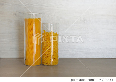 Pasta in large glass jars containers stand on gray table in kitchen. Uncooked raw italian pasta with spaghetti. 96702833