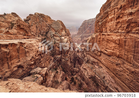 Typical landscape at Petra, Jordan, rocky walls around narrow canyon, few small bushes growing in red dusty ground Typical landscape at Petra, Jordan, rocky walls around narrow canyon, few small bushes growing in red dusty ground 96703918