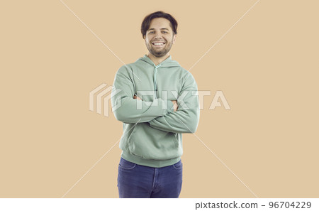 Portrait of happy smiling brunet man in mint hoodie and jeans on beige background looking at camera. 96704229