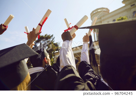 College or university graduates holding up their diplomas during graduation ceremony College or university graduates holding up their diplomas during graduation ceremony 96704245