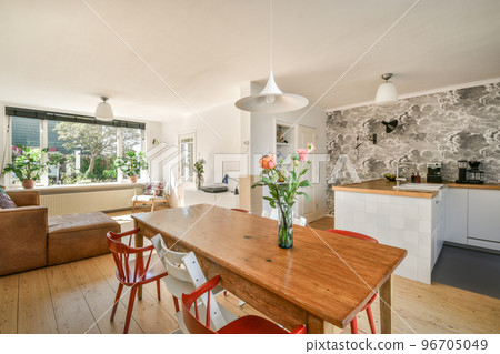 Table with chairs and flowers located near lounge area and kitchen in spacious room of contemporary apartment 96705049