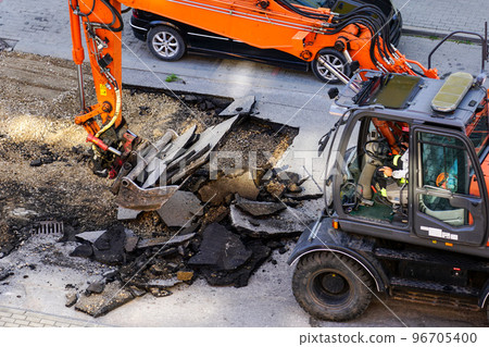 An excavator breaks up the old asphalt layer with a bucket during street repairs An excavator breaks up the old asphalt layer with a bucket during street repairs 96705400