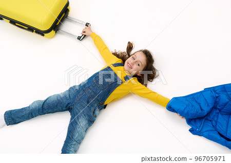 Top view cute little child girl tourist in blue denim overalls, with yellow sweater and suitcase, lying on white background, advertising space. Travel abroad. Getaway. Air flight trip journey concept Top view cute little child girl tourist in blue denim overalls, with yellow sweater and suitcase, lying on white background, advertising space. Travel abroad. Getaway. Air flight trip journey concept 96705971