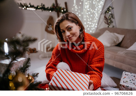 Portrait of the cute woman holding present near Christmas tree at the cozy evening 96706626