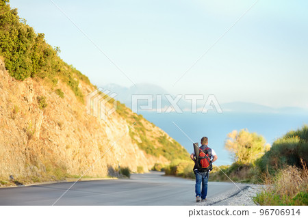 Mature man hiking on mountains nearby sea. Person walking along road. Concepts of adventure, extreme survival, orienteering. Hitch-hiking. Solo travel. Backpacking trip. 96706914
