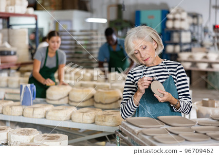 Mature woman processing new clay plates in workshop Mature woman processing new clay plates in workshop 96709462