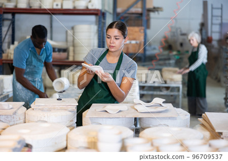 Happy female sculptor checks quality of designer clay plates 96709537