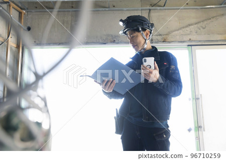 A worker man looking at a file while operating a smartphone at a construction site 96710259