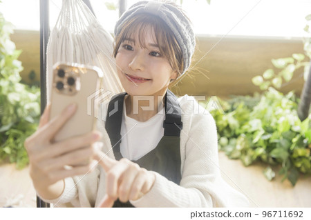 A young woman sitting in a hammock and looking at her smartphone Home Camping Camping Image 96711692